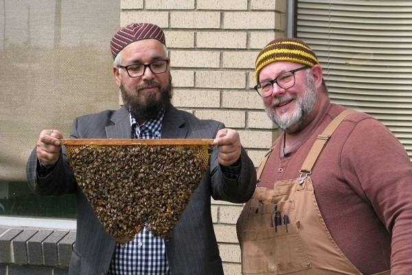 Masjid Al Qur’an Imam Hafiz Muhammad Shafiq holds up a honey comb as bee expert Charlie Koenen of BeeVangelists stands by.
