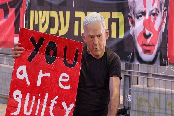 A demonstrator wearing a mask representing the Israeli regime's prime minister Benjamin Netanyahu lifts a placard during an anti-government protest in Tel Aviv on August 31, 2024