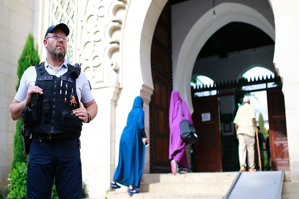 Muslims entering the Grand Mosque of Paris as a police officer is standing guard.