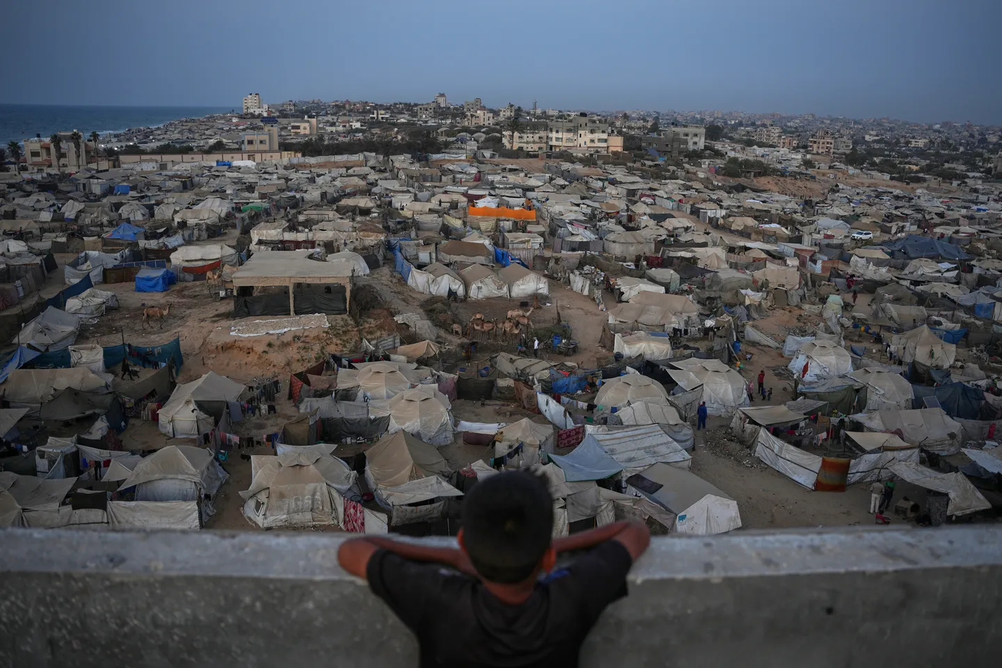 A boy looks at a makeshift tent camp for displaced Palestinians stretching across an area in Zawaida, in central Gaza.