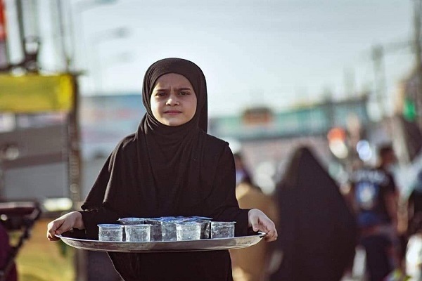 An Iraqi girl serves beverages to Arbaeen pilgrims